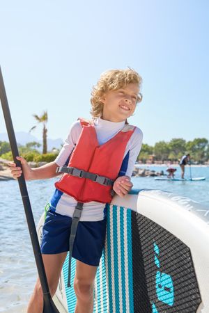 Cheerful boy with paddleboard on seashore