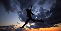 Out line of male jumping in the splits against a colorful dusk side