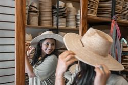 A young Hispanic woman is looking in the mirror trying a new hat