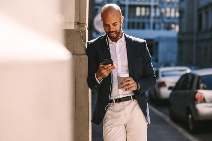 Handsome businessman leaning on a wall while standing outdoors and using smartphone