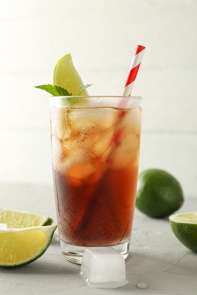 Glass with cold cola and citrus on grey cement background, space for text