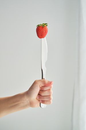 Crop person showing strawberry pricked on knife