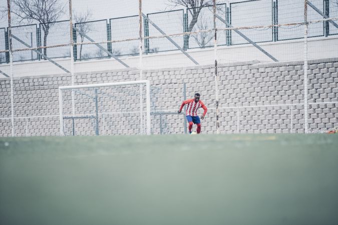 Black soccer player with red equipment playing soccer.