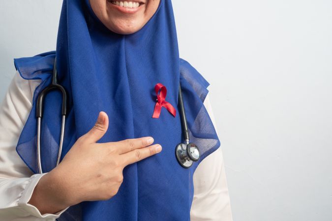 Happy Muslim Female Asian doctor or nurse pointing Red ribbons on cloth, HIV awareness concept, world AIDS day, world cancer day.