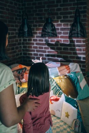 Unrecognizable woman and girl having fun together playing in shade show on living room