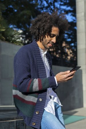 Smiling Black man using his smartphone while leaning outside in the sun