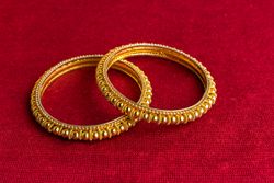Beautiful shiny golden bangles with Indian traditional design on a red velvet background