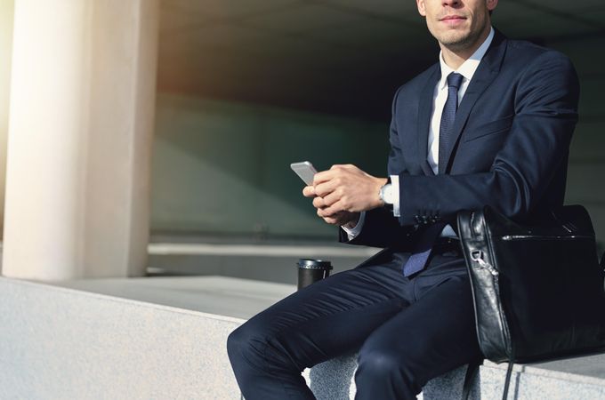 Man in business attire holding cell phone with leather computer bag