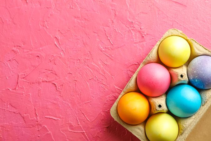Decorative eggs in cardboard box on color background, space for text. Top view