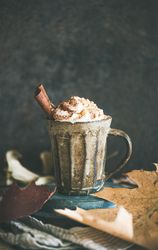 Mug of warm drink topped with whipped cream and cinnamon sticks, copy space