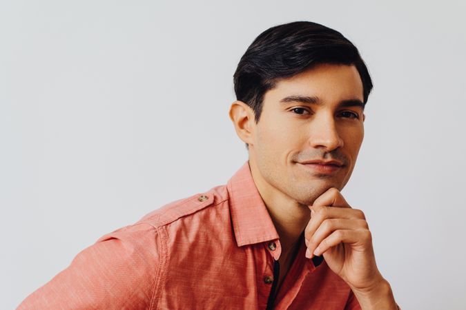 Headshot of curious Hispanic male looking at camera in grey studio, copy space