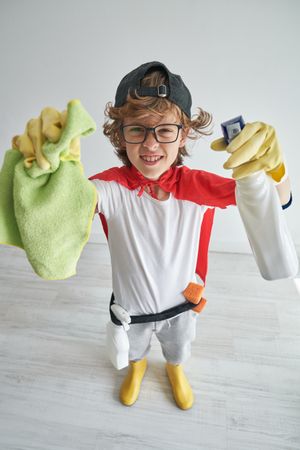 Smiling boy standing with house cleaning items and looking at ca