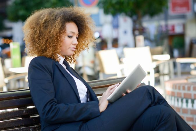 Serious woman in suit reading something on her digital tablet on outdoor bench