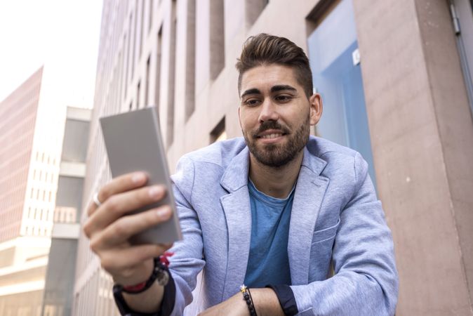 Portrait of happy man smiling while using his mobile phone standing outside