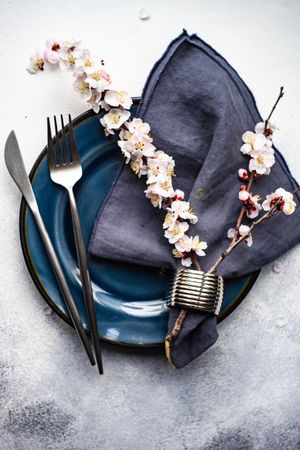 Table setting with delicate apricot blossom around elegant navy tableware on grey counter