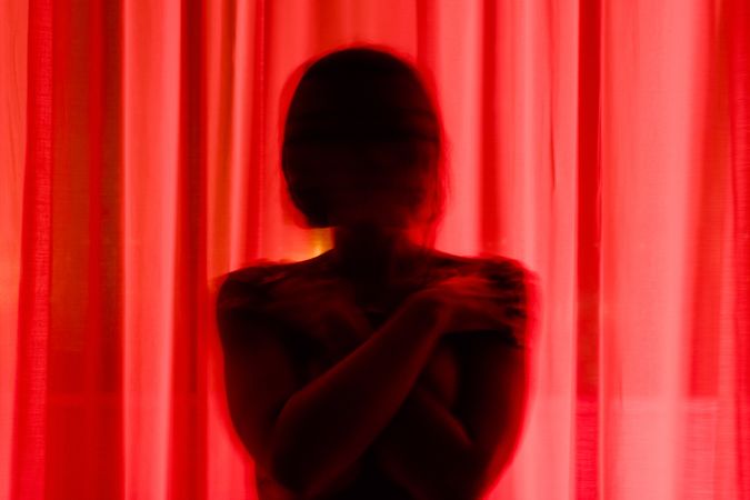 Faceless person hiding behind curtains at night time