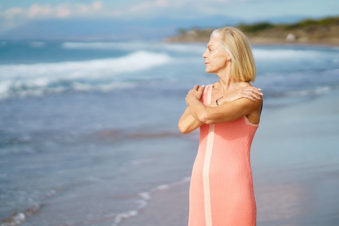 Calm older woman smiling while standing in the sand on a beach