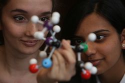 Two young women look at a molecule model 0g9R84