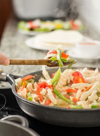 Female cooking vegetables and chicken in pan