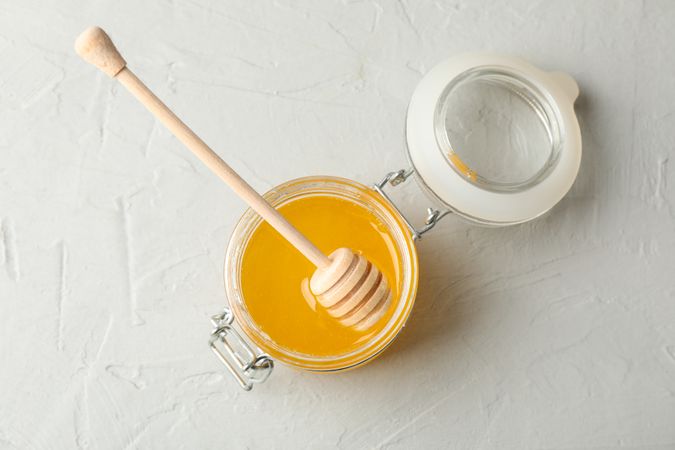Glass jar with honey and dipper on neutral background, top view