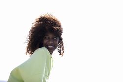 Smiling female with curly hair in bright green shirt against sunny sky with space for text