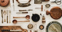Vintage kitchen utensils and knifes artfully arranged on beige tablecloth, wide composition