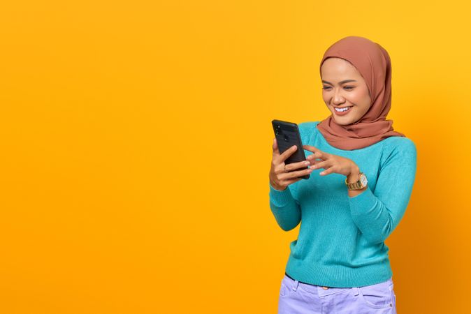 Smiling Muslim woman sending text from her smartphone