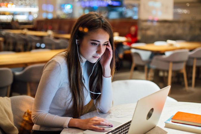 Hard working brunette woman in a restaurant working on her laptop with earbuds