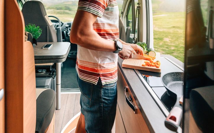 Male chopping vegetables in motorhome kitchen with open door