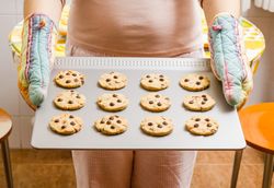 Woman holding a tray with baked cookies with kitchen gloves