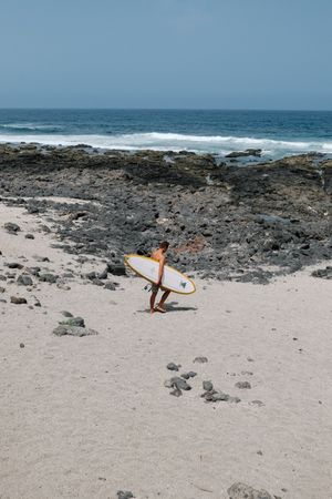 Man walking towards beach with yellow surfboard