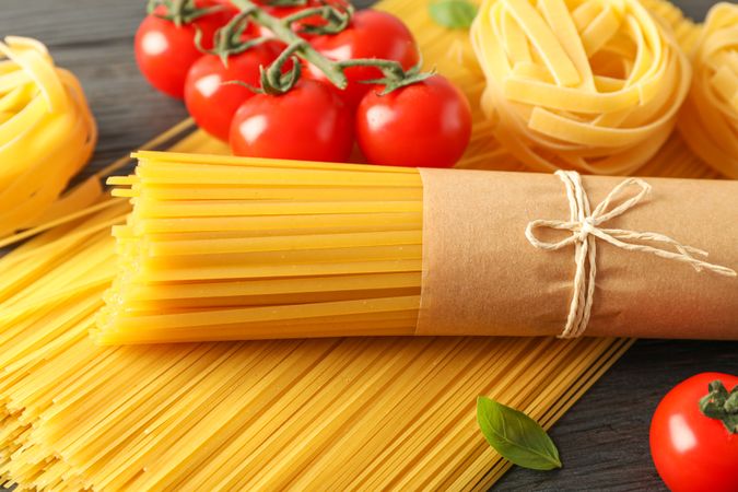 Composition with pasta, tomatoes and basil on wooden background, space for text and closeup