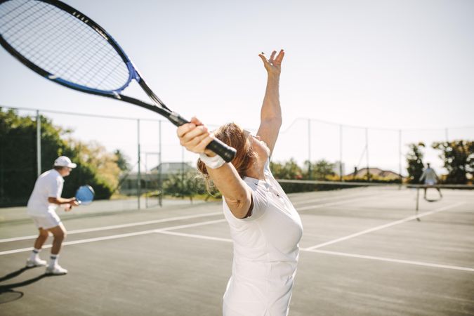 Action shot of woman tossing ball up to serve with her tennis racket