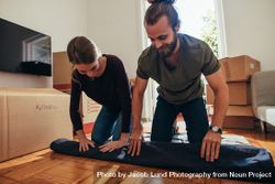 Couple working together to roll up a carpet on floor for packing 0L9ve5