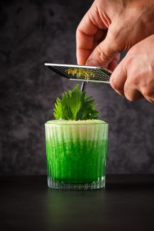 Anonymous barman decorating green cocktail with grated camomile