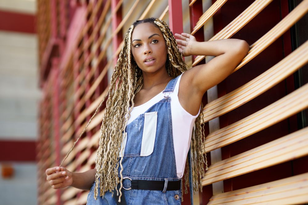 Female in vest and overalls posing on window blinds, low angle