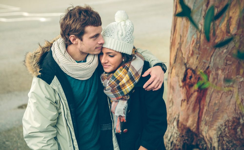 Affectionate couple in winter coats embracing under tree