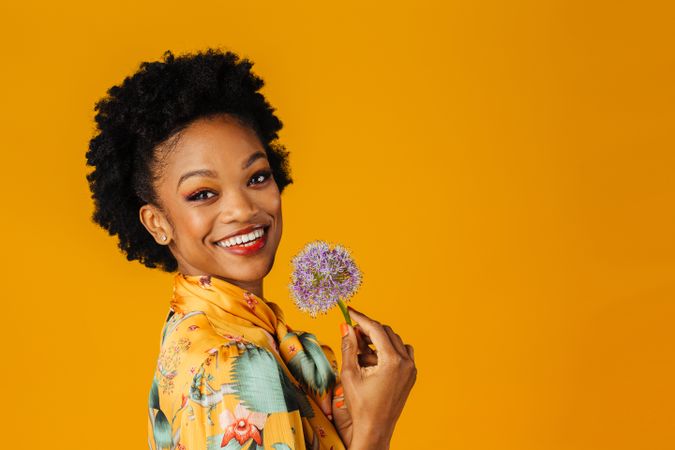 Smiling Black woman holding purple flower to her face