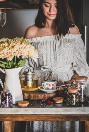 Woman in rustic kitchen with teapot brewing and floral tea cup