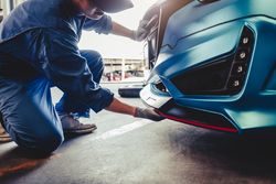 Car mechanic crushing next to car checking bumper