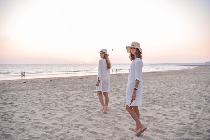 Smiling girlfriends in summer clothes barefoot in water on beach