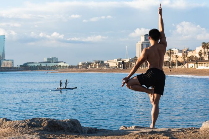 Shirtless man balancing in yoga pose on beach