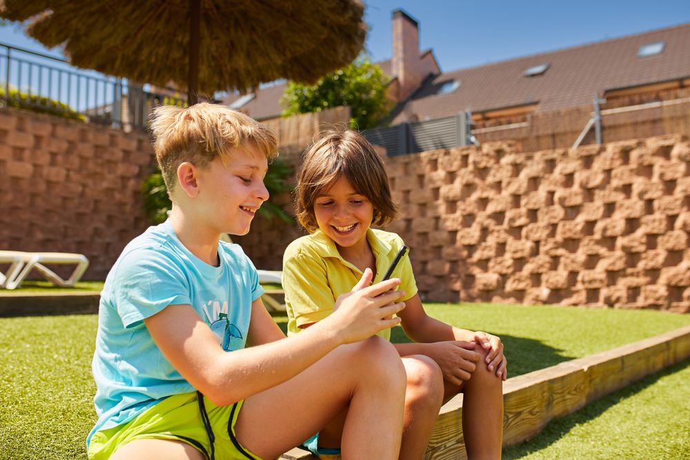 Cheerful boys browsing smartphone sitting on garden