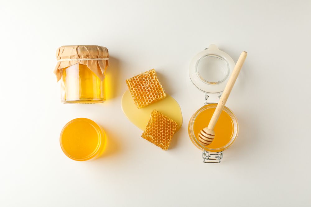 Flat lay. Jars with honey, dipper and honeycomb on neutral background