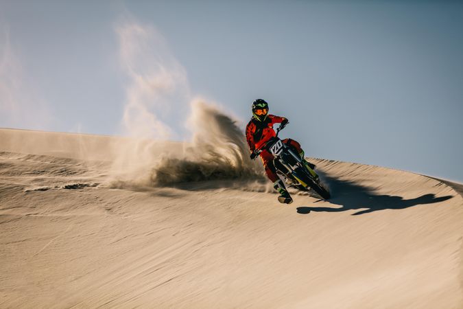 Dirt biker going full throttle over sand dunes