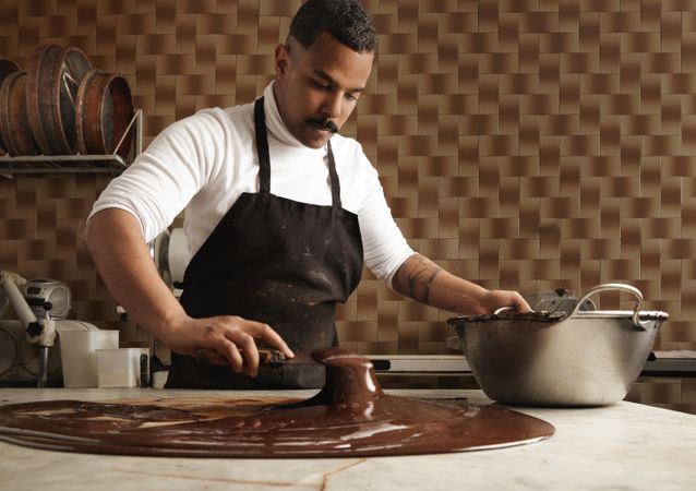 Man in apron molding melted chocolate in professional kitchen