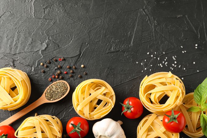 Flat lay composition with pasta, tomatoes, salt, garlic and spices on dark background, space for text