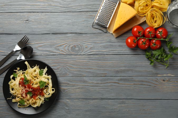 Composition with plate of tasty pasta and ingredients for cooking on wooden background