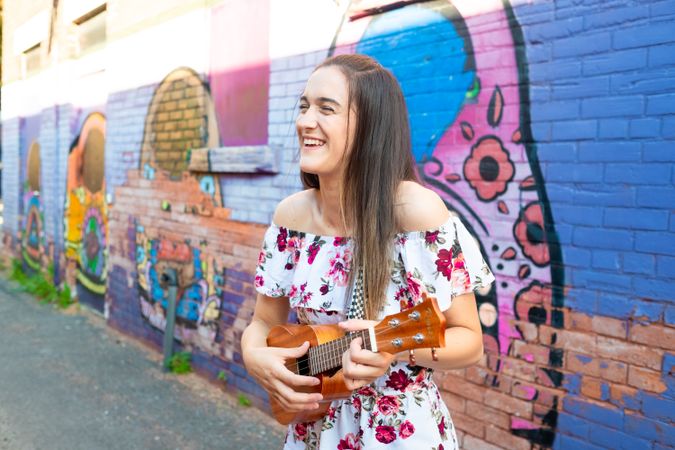 Joyful woman playing ukulele while standing on urban street