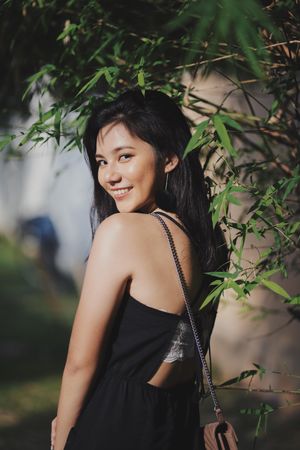 Side view of smiling woman in dark dress posing under a tree